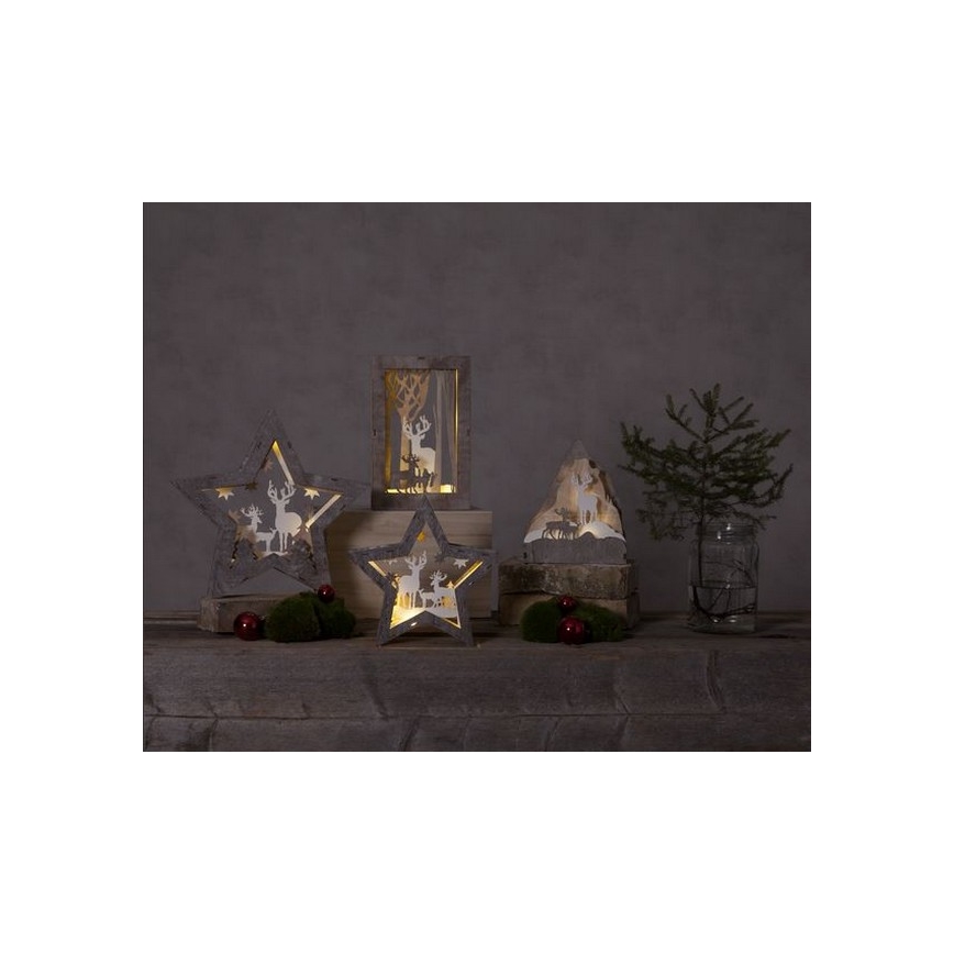 Drevené hviezdne a obdĺžnikové svietniky s vyrezávanými jelenmi svietia. Stoja na drevenom podklade s ihličnatým stromčekom a ozdobami.