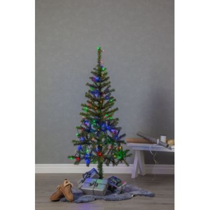 Vianočný stromček s farebnými svetielkami stojí na kožúšku pred bielou lavicou v miestnosti. Pod stromčekom sú darčeky.