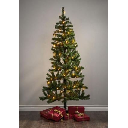 Vianočný stromček s teplými svetielkami stojí na podlahe pred svetlou stenou. Pri jeho spodnej časti sú červené darčekové balíčky previazané zlatými stužkami.