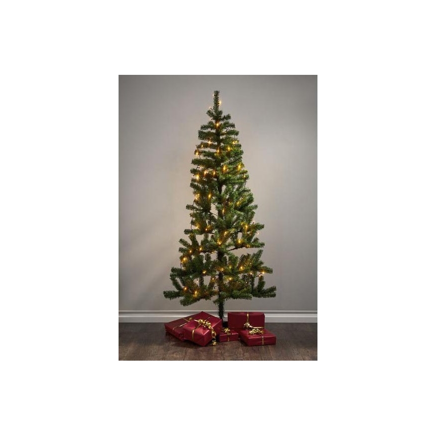 Vianočný stromček s teplými svetielkami stojí na podlahe pred svetlou stenou. Pri jeho spodnej časti sú červené darčekové balíčky previazané zlatými stužkami.