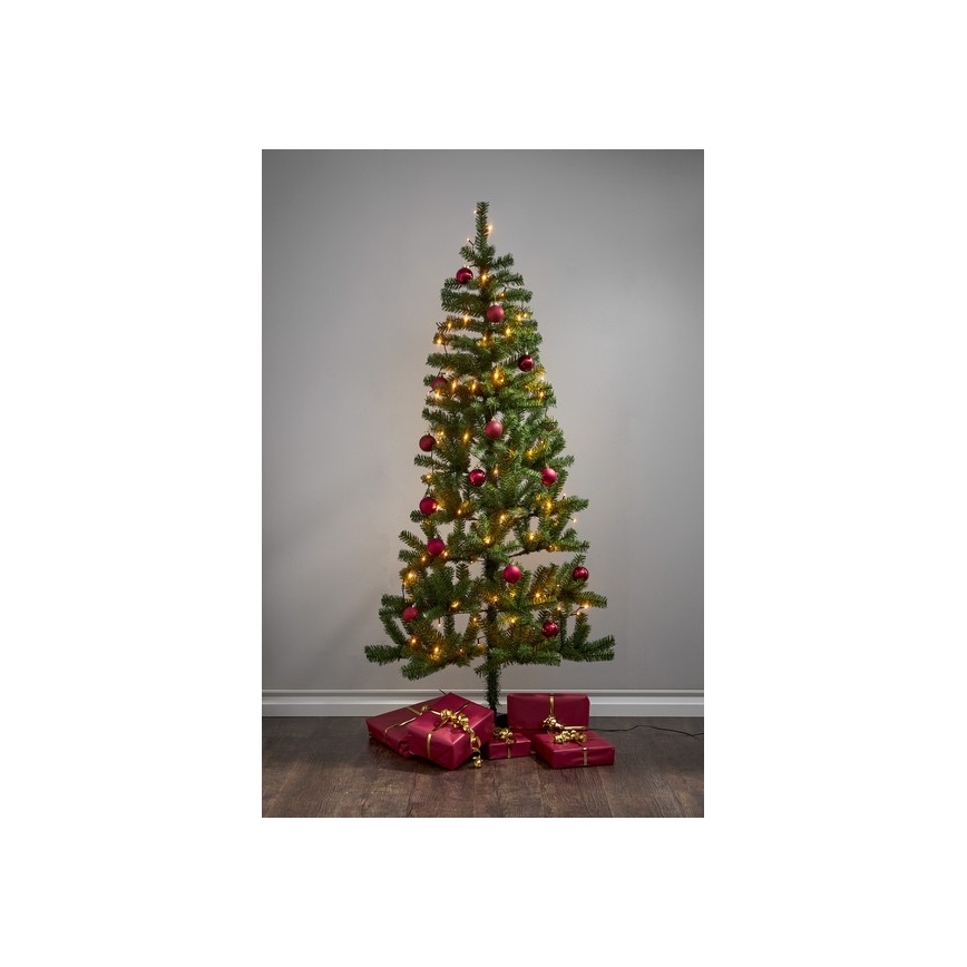 Vianočný stromček s červenými guľôčkami a svetielkami stojí na podlahe pred šedou stenou. Pri jeho spodnej časti sú umiestnené červené darčekové balíčky previazané zlatou stuhou.