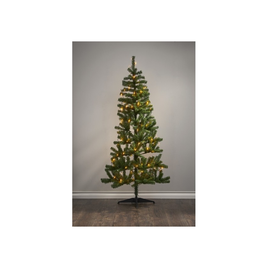 Vianočný stromček s teplými svetielkami stojí na podlahe pred svetlou stenou. Stromček je ozdobený svetelným girlandou.