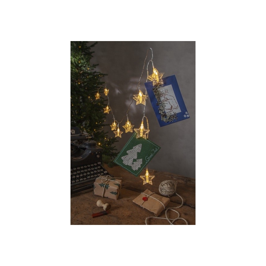 Svetelná reťaz s hviezdičkovými LED diódami drží pohľadnice. Na stole je starý písací stroj, balíčky a špagát. Pohľadnice obsahujú text „God Jul“.