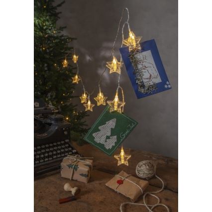 Svetelná reťaz s hviezdičkovými LED diódami drží pohľadnice. Na stole je starý písací stroj, balíčky a špagát. Pohľadnice obsahujú text „God Jul“.