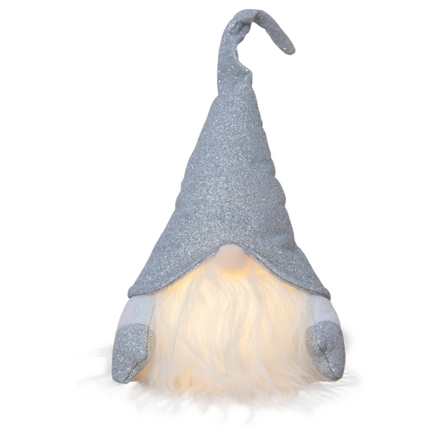 Svietnica v tvare škriatka sedí na bielom pozadí. Škriatok má strieborný trblietavý klobúk a biely fúzik, ktorý svieti. Jeho rukávy sú tiež strieborné a trblietavé.