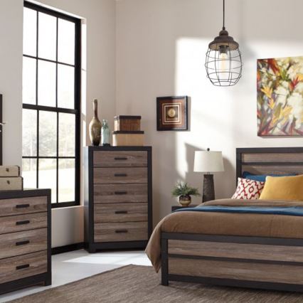 Závesná lampa visí v spálni. Lampa s kovovou klietkou osvetľuje posteľ s hnedým čalúnením a komodu. V pozadí je veľké okno.