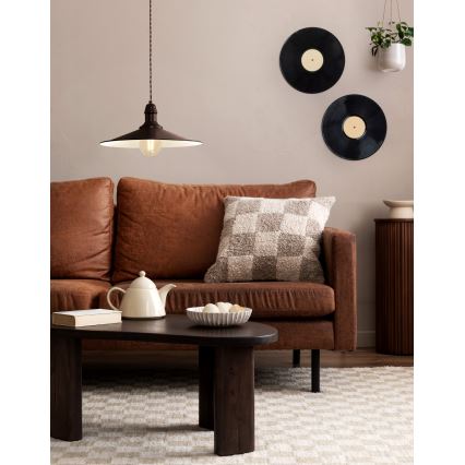 Kožená sedačka s vankúšom – stojí v obývacej izbe, na ktorej je konferenčný stolík s kanvicou a miskou. Nad sedačkou visí lustre. Na stene sú dve gramofónové platne.