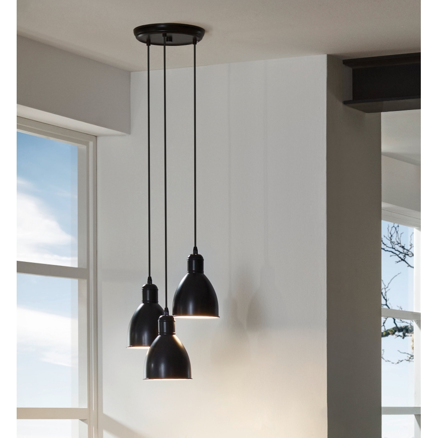 Trojramenné čierne závesné svietidlo visí zo stropu. Svietidlo má tri kužeľovité tienidlá. Kontext tvorí svetlá miestnosť s oknom.