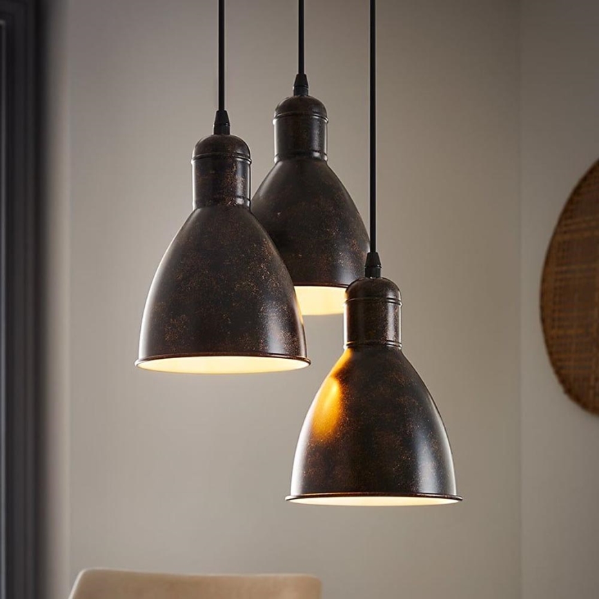 Trojica hnedých kovových svietidiel svieti v interiéri. Svietidlá visia z čiernych káblov. Na pozadí je viditeľná časť steny a nábytok.