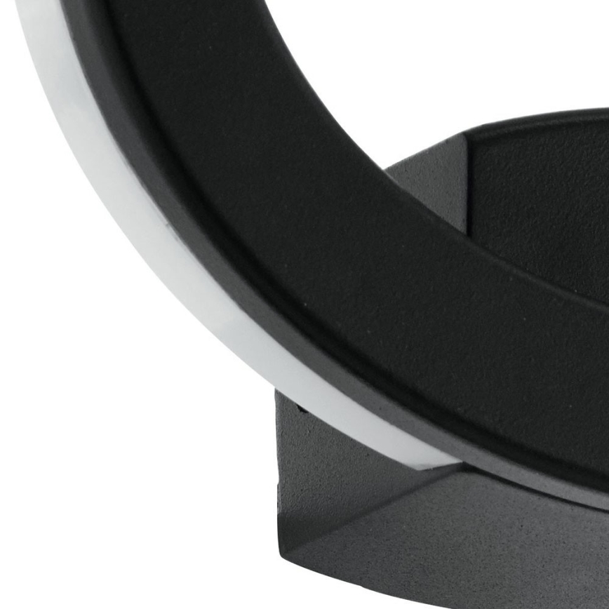 Svietidlo v tvare polkruhu, pripevnené k stene, vyžaruje svetlo. Jeho základňa je tmavosivá, polkruh je čierno-strieborný.