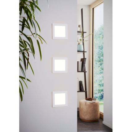 Tri štvorcové nástenné LED svetlá sú namontované na stene. Svietia v interiéri blízko knižnice a okna.