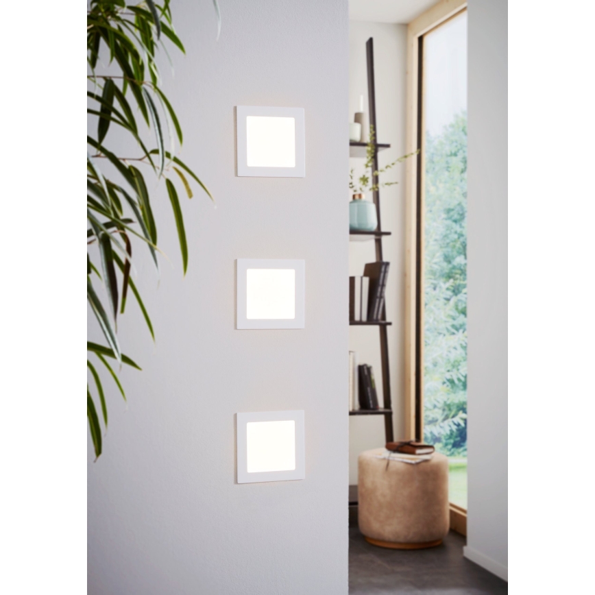 Tri štvorcové nástenné LED svetlá sú namontované na stene. Svietia v interiéri blízko knižnice a okna.