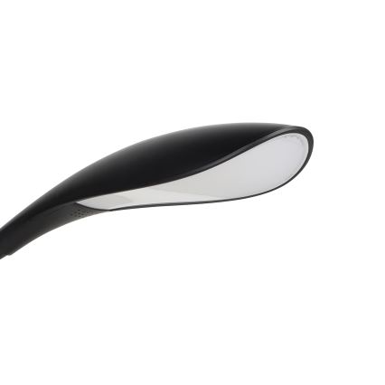 Stolová lampa s čiernym telom a bielym difúzorom svieti. Lampa je zakrivená a má moderný dizajn. Je umiestnená na bielom pozadí.