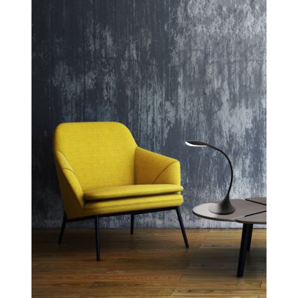 Žltý kreslo stojí v miestnosti s betónovou stenou. Na nízkom stolíku pred ním sa nachádza čierna stolová lampa s zahnutým ramenom.