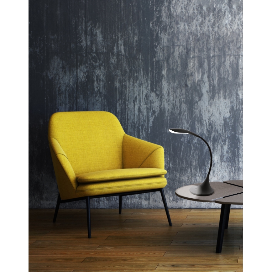 Žltý kreslo stojí v miestnosti s betónovou stenou. Na nízkom stolíku pred ním sa nachádza čierna stolová lampa s zahnutým ramenom.