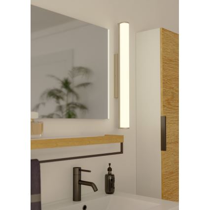 Svetlo svieti v kúpeľni. Je pripevnené na stene vedľa zrkadla a drevenej poličky s umývadlom.