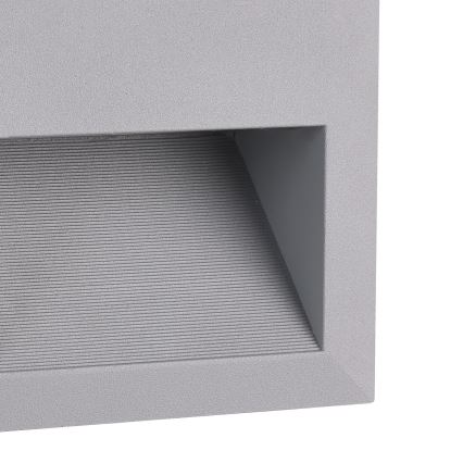 Svietidlo svieti. Je umiestnené v šedej obdĺžnikovej konštrukcii s ryhovaným povrchom.