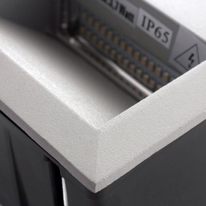Svetlošedá nástenná svítidlo s LED diódami je čiastočne zapustená do tmavosivej montážnej skrinky. Na svätidle je viditeľné označenie IP65.