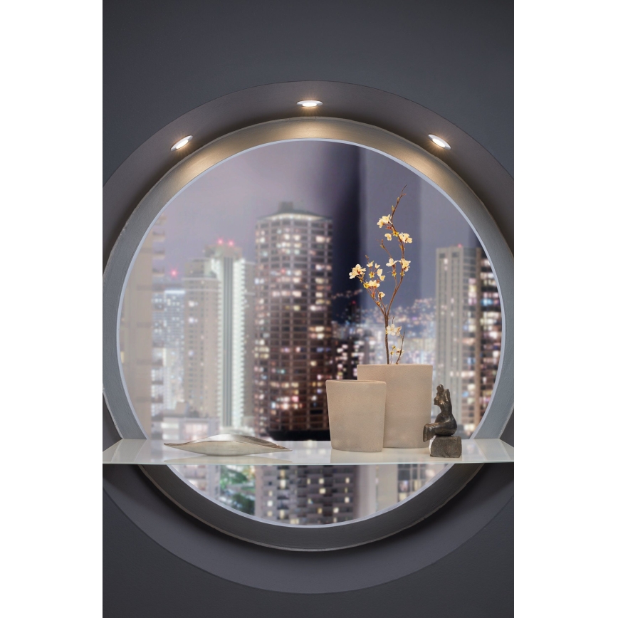 Kvetináč s kvetmi stojí na poličke s dekoratívnym predmetom a soškou. Polička je osvetlená a umiestnená v okrúhlom výklenku s výhľadom na nočné mesto.