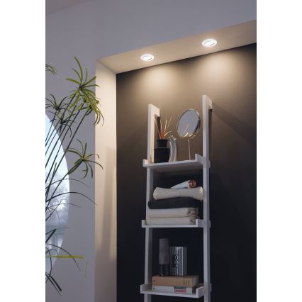 Svietidlá osvetľujú bielu poličku s uterákmi, doplnkami a knihami v kúpeľni.