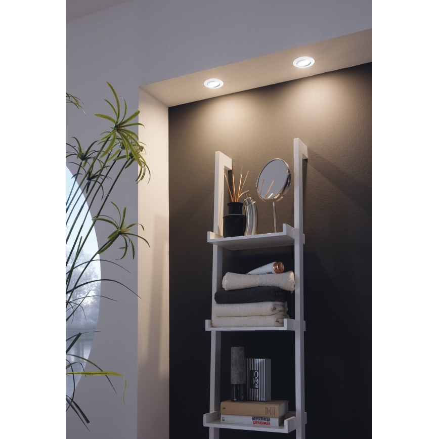 Svietidlá osvetľujú bielu poličku s uterákmi, doplnkami a knihami v kúpeľni.