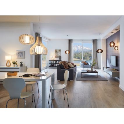 Drevené závesné lampy svietia v modernej jedálni a obývacej izbe s drevenou podlahou a výhľadom na hory. Stôl s bielymi stoličkami je v popredí, za ním je sedacia súprava a televízor.