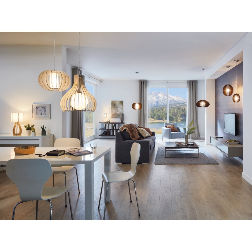Drevené závesné lampy svietia v modernej jedálni a obývacej izbe s drevenou podlahou a výhľadom na hory. Stôl s bielymi stoličkami je v popredí, za ním je sedacia súprava a televízor.