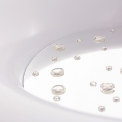 Kvapky vody ležia na lesklej bielej ploche. Voda je priesvitná a rozložená nerovnomerne. Plocha je súčasťou väčšieho bieleho predmetu.