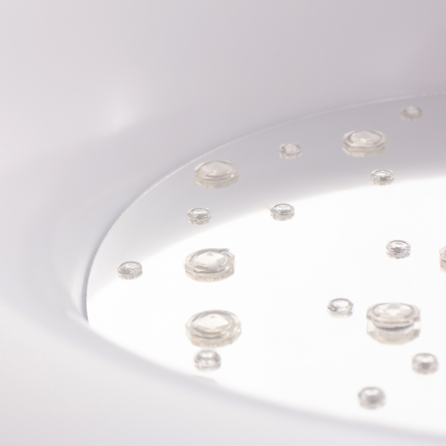 Kvapky vody ležia na lesklej bielej ploche. Voda je priesvitná a rozložená nerovnomerne. Plocha je súčasťou väčšieho bieleho predmetu.