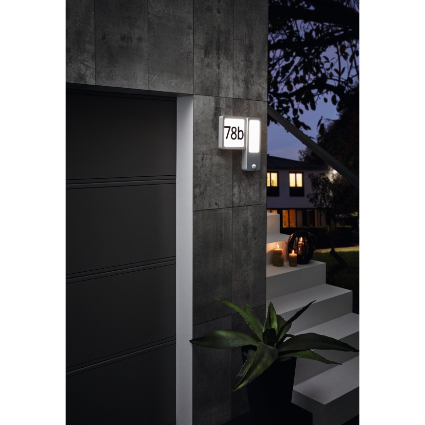 Svietidlo s číslom 78b je namontované na stene vedľa garážových dverí. Svietidlo svieti v noci. V pozadí sa nachádzajú schody a okolitá záhradná architektúra.