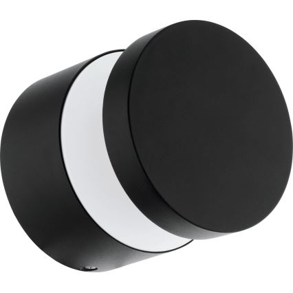 Čierna nástenná lampa s valcovým tvarom a bielym difúzorom vyžaruje svetlo. Lampa je otočená mierne do strany. Je umiestnená na bielom pozadí.