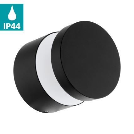Čierna nástenná lampa svieti. Je valcovitého tvaru s okrúhlou svetelnou časťou. Stupeň krytia IP44.