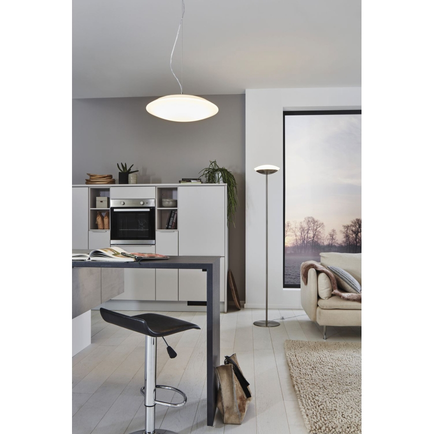 Závesné svietidlo svieti v kuchyni s kuchynským ostrovčekom a barovou stoličkou. V miestnosti je tiež stojacia lampa a pohovka.