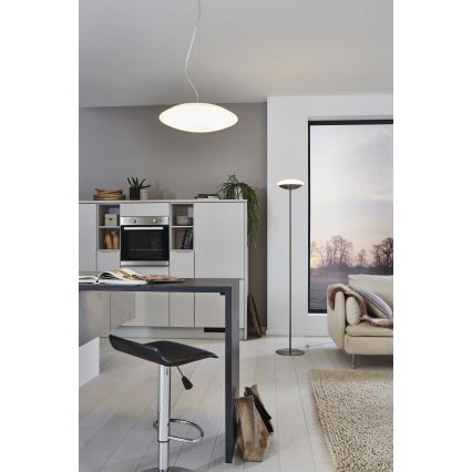 Závesné svietidlo svieti v kuchyni s kuchynským ostrovčekom a barovou stoličkou. V miestnosti je tiež stojacia lampa a pohovka.