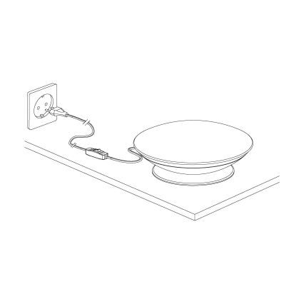 Ploché kruhové svetlo je pripojené káblom k elektrickej zásuvke cez vypínač. Svetlo stojí na povrchu stola.