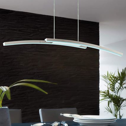 Dvojité krivočiare LED svietidlo visí nad jedálenským stolom. Svietidlo je upevnené na strope a osvetľuje tmavosivú stenu a stôl s riadom.