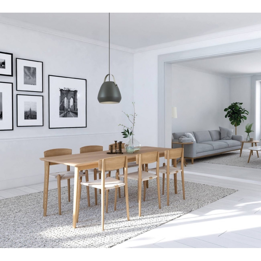 Drevený jedálenský stôl s priľahlými stoličkami stojí na svetlom koberci. Nad stolom visí šedá závesná lampa. V pozadí je viditeľná sivá sedačka a ďalší nábytok v svetlom interiéri.