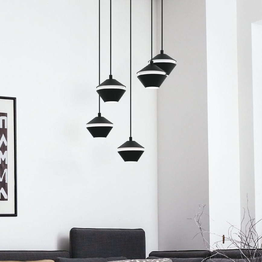 Štyri čierne závesné lampy s bielym vnútorným kruhom visia z bielej steny v miestnosti s tmavosivou sedačkou. Lampy sú rôznej veľkosti.