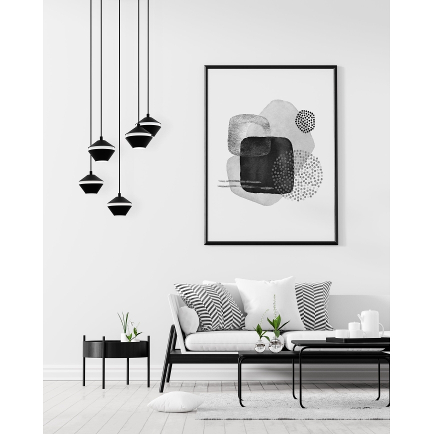 Čierne závesné lampy s tvarom obráteného kužeľa visia v minimalistickej obývacej izbe s bielym gaučom a abstraktným čierno-bielym obrazom na stene.