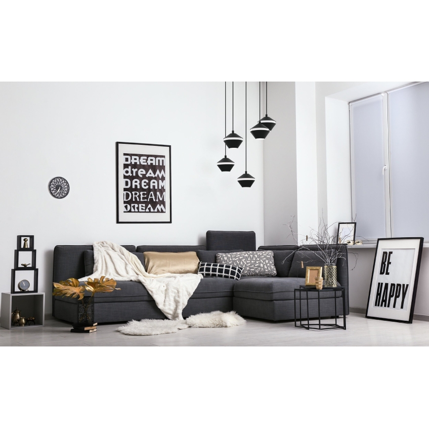 Sivá rohová sedačka stojí v obývacej izbe. Na stene visia obrazy s textom: „DREAM dream DREAM DREAM DREAM“ a „BE HAPPY“. Nad sedačkou visia tri čierne závesné lampy.