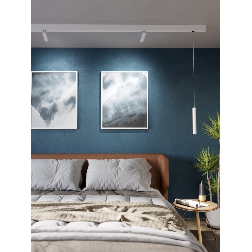Dve stropné svietidlá osvetľujú posteľ s posteľnou bielizňou a dvomi obrazmi s abstraktnou krajinou na modrej stene. Visiace svietidlo dopĺňa osvetlenie.