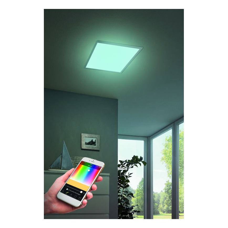 Štvorcový stropný LED panel svieti svetlom tyrkysovej farby. Panel sa ovláda smartfónom zobrazujúcim farebnú paletu a nastavenie intenzity. Panel je umiestnený v miestnosti s oknami a rastlinou.