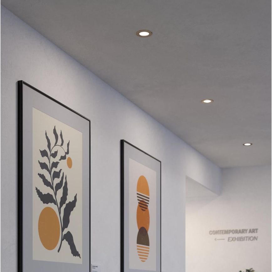 Dva obrazy s abstraktnou grafikou visia na stene chodby. Na strope sú zabudované bodové svetlá. Na stene je nápis: „CONTEMPORARY ART ← EXHIBITION“.