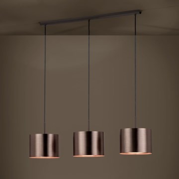 Trojité závesné svietidlo s valcovými tienidlami v bronzovej farbe visí zo spoločnej stropnej lišty. Tienidlá sú zavesené na čiernych kábloch v neutrálnej hnedej miestnosti.