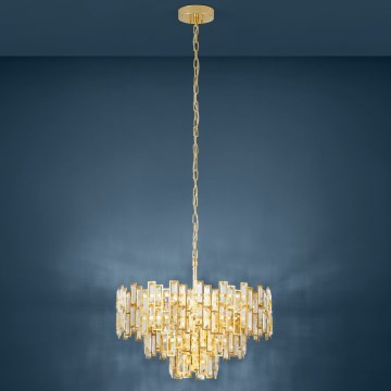 Zlatý luster s kryštáľovými prvkami visí zo stropu. Je zavesený na zlatom reťazi. Pozadím je tmavomodrá stena.