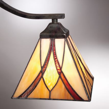 Vitrážový tienidlo pyramídového tvaru so žlto-červenými geometrickými vzormi visí na zakrivenej kovovej lampe.