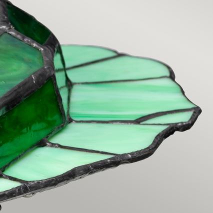 Vitrážová tienidlo z tmavozeleného a svetlozeleného skla je spojené čiernou kovovú štruktúrou. Tienidlo má tvar kvetu, pričom jeho okraje sú nepravidelné.