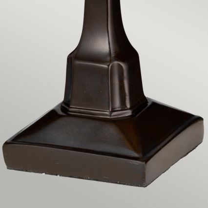 Tmavohnedá podstavec s hranatou základňou stojí na svetlom podklade. Je vyrobený z hladkého materiálu s výraznými líniami.