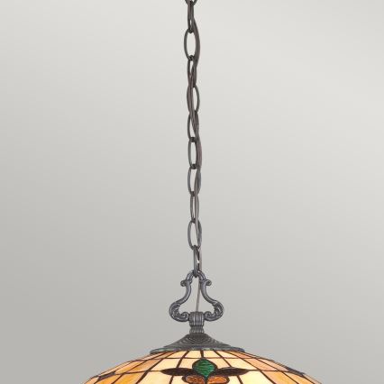 Závesná lampa s tienidlom z vitráže visí na reťazi. Tienidlo je okrúhle, béžovo-žlté s hnedými a zelenými detailmi. Lampa je zavesená na svetlom pozadí.
