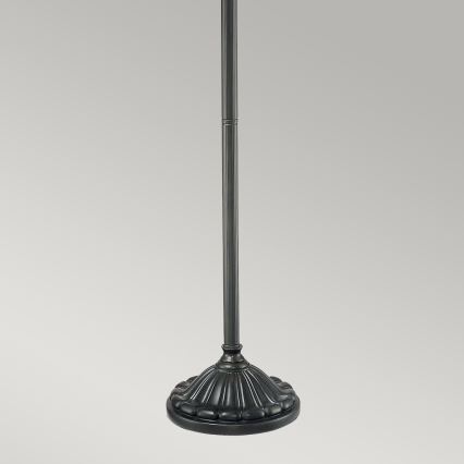 Stojanová lampa stojí na rovnom povrchu. Je tmavosivej farby a má ozdobnú podstavu. Stĺpik lampy je hladký a rovný.